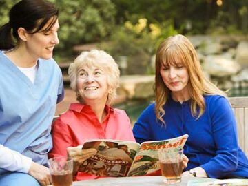 three people sitting at table and holding a magazine in front have a drinks