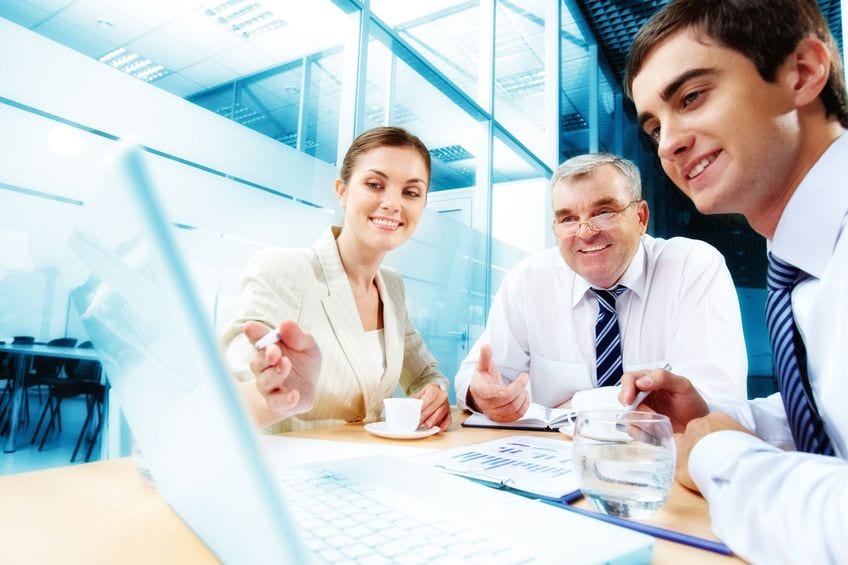 A group of people sitting together at table in front of laptop